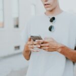 man in white crew-neck top using smartphone outdoors